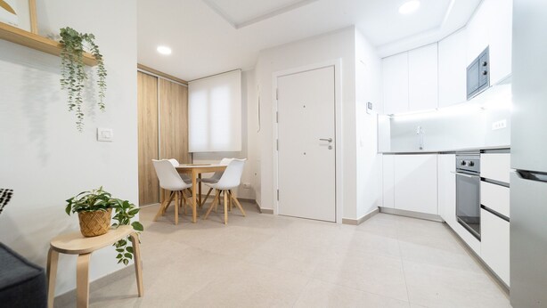 Una cocina moderna con armarios blancos, horno empotrado y microondas. Hay un comedor con mesa y sillas.