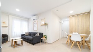 Una sala moderna con un sofá gris, una mesita redonda y un comedor con una mesa y sillas blancas.