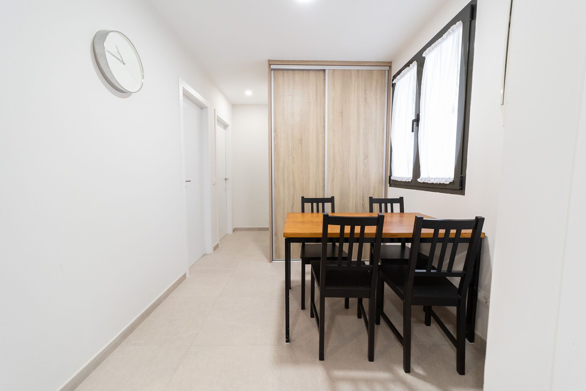Un pasillo con una mesa de comedor de madera y sillas, un reloj en la pared y una puerta corredera.