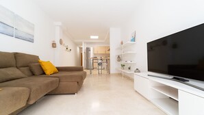 Una sala de estar moderna con un sofá, televisión y una cocina al fondo.