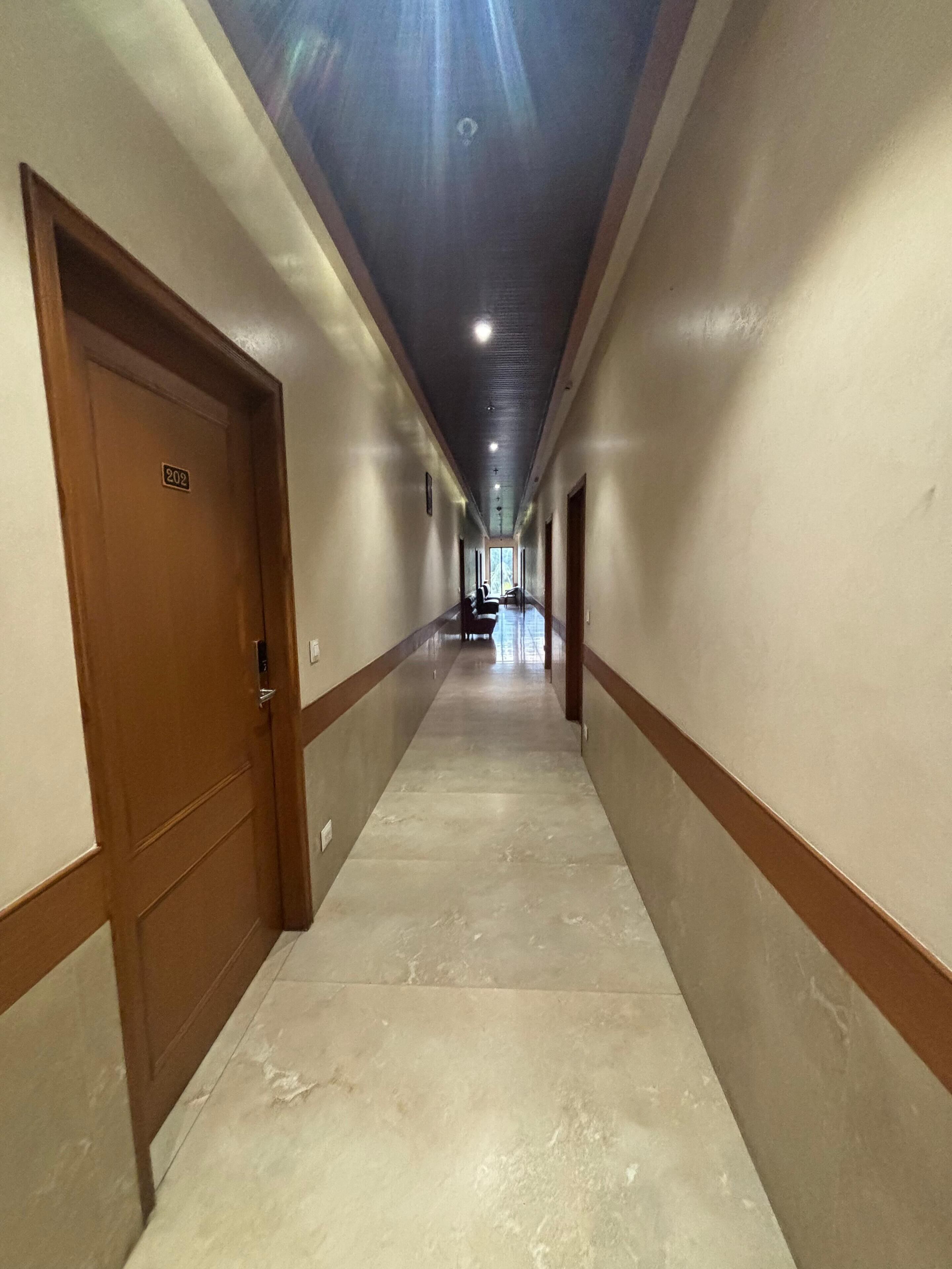 A long, narrow hallway with marble flooring and wooden doors on both sides.