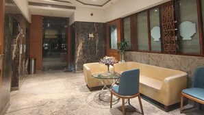 A lobby with a marble floor, a glass coffee table, a sofa, and a chair. - Shelter Suites (Formerly known as Fisco The Hub Link) (Mumbai)