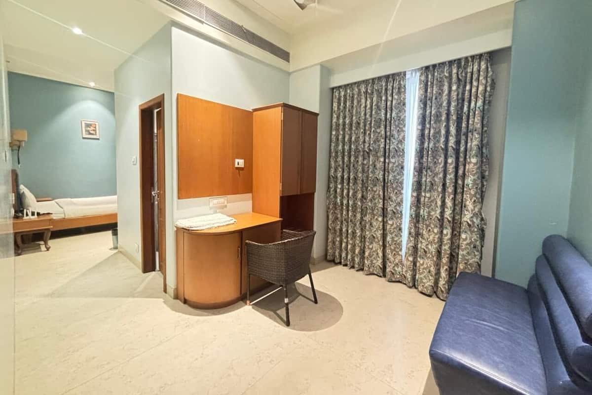 Habitación de hotel con cama, escritorio, silla, sofá y ventana con cortinas.