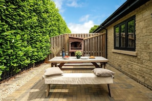 Une terrasse avec une table en bois, deux bancs et un mur en briques.