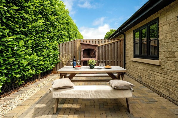 A patio with a wooden table, two benches, and a brick wall.