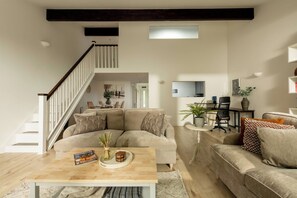 A modern living room with a sectional sofa, a coffee table with magazines, a staircase, and a dining area in the background.
