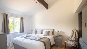 A bedroom with a large bed, bedside tables, a chair, and a window with curtains. - York Cottage (South Cerney)