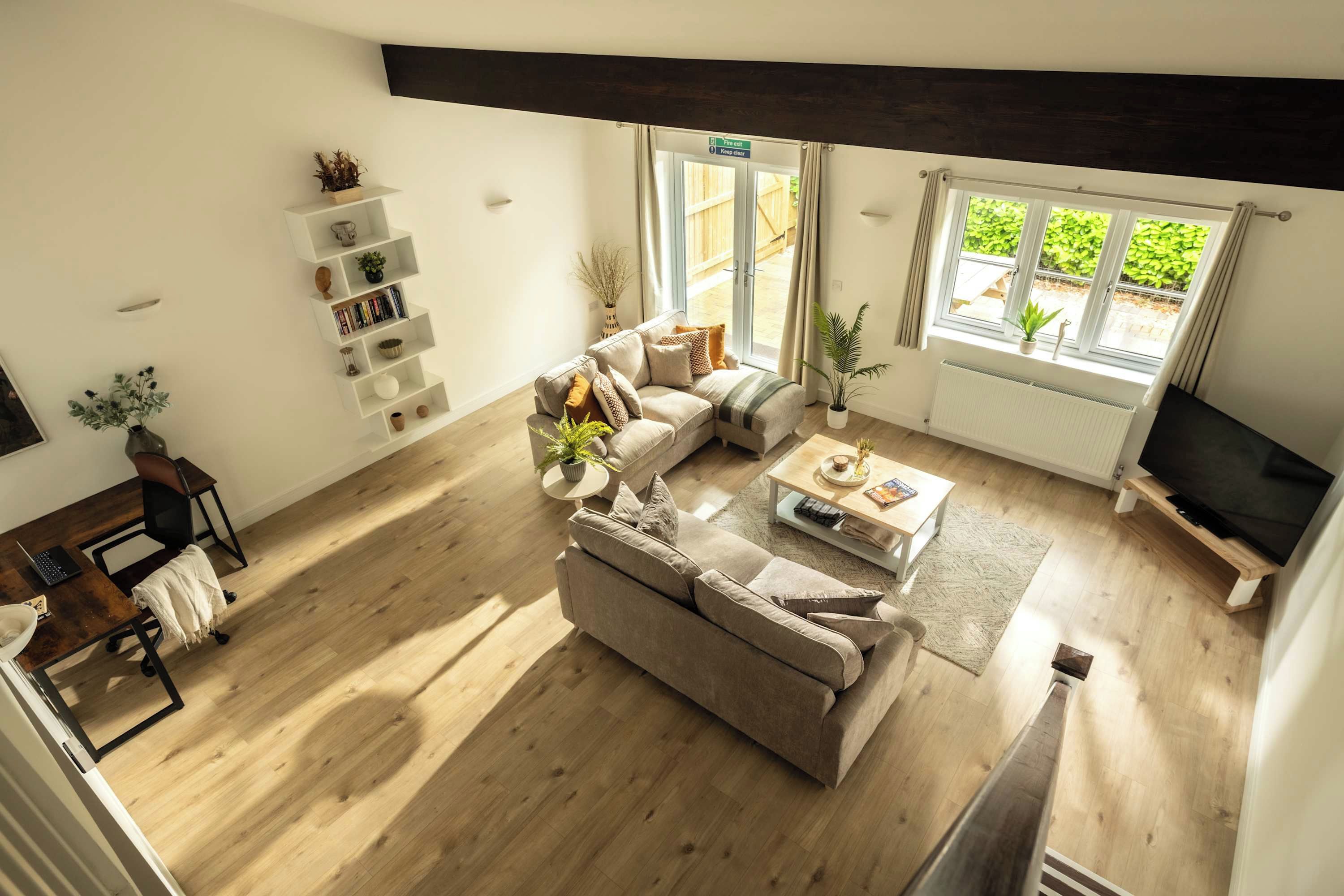 A modern living room with a sofa, coffee table, and TV. There is a bookshelf and a window with a view of greenery.