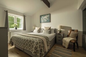 Une chambre à coucher comprenant un lit, des tables de chevet, une chaise, une fenêtre avec des rideaux, un radiateur et un tableau accroché au mur.