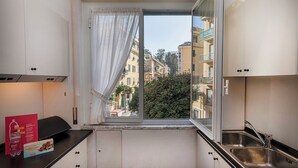 A compact kitchen with a window view of a cityscape, a sink, and cabinets. - Large Apartment in the Heart of Santa Margherita Ligure by Wonderful Italy (Santa Margherita Ligure)