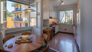 A compact kitchen with a dining area, large windows, and a view of neighboring buildings. - Large Apartment in the Heart of Santa Margherita Ligure by Wonderful Italy (Santa Margherita Ligure)