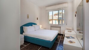 A bedroom with a bed, bedside tables, a desk, a mirror, and a window with a view of buildings. - Large Apartment in the Heart of Santa Margherita Ligure by Wonderful Italy (Santa Margherita Ligure)