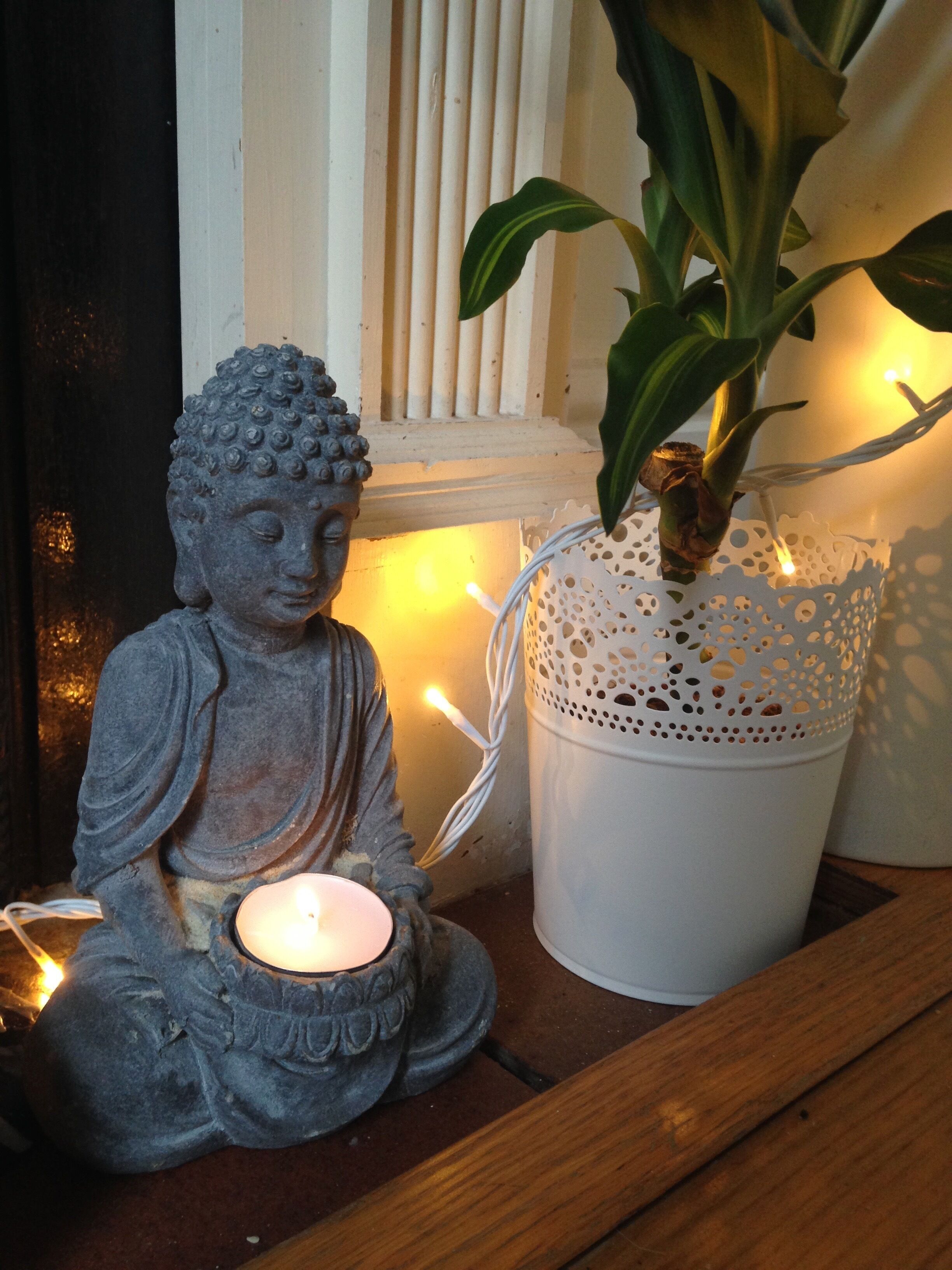 A Buddha statue with a lit candle, a potted plant, and a white basket with a candle inside.