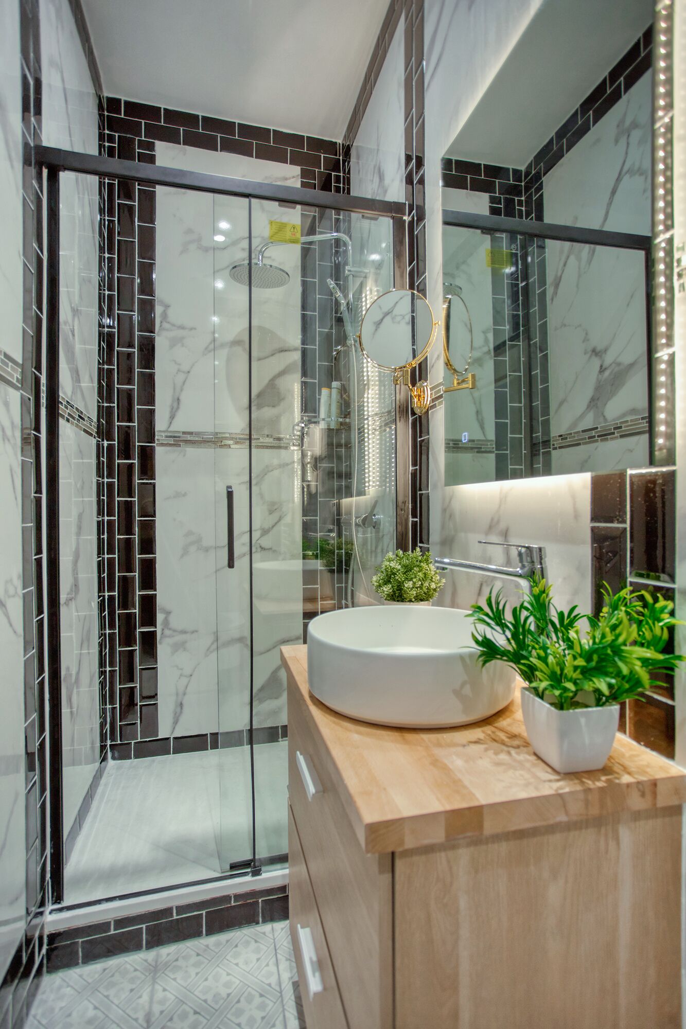 A modern bathroom with a glass-enclosed shower, a round sink, and a mirror with lights.
