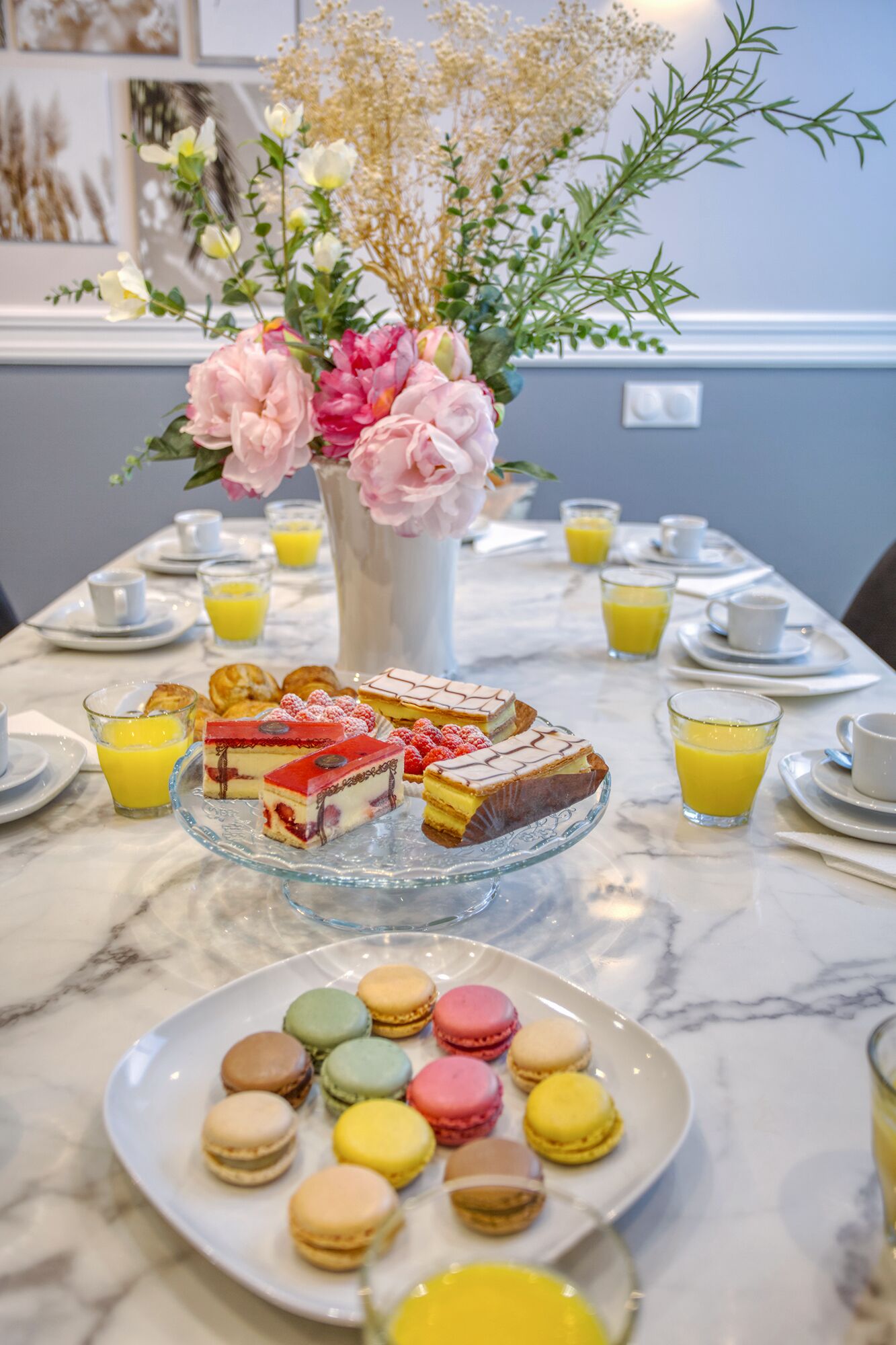Una mesa de desayuno con pasteles, macarons y un florero de flores.