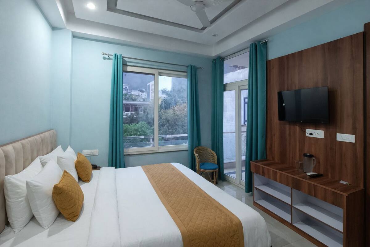 Quarto de hotel com cama, televisão, poltrona e vista para o exterior.