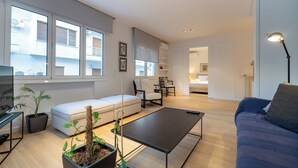 A modern living room with a sofa, a coffee table, and potted plants. There is a dining area with a table and chairs.