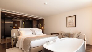 A modern hotel room with a large bed, a bathtub, a small table, and a chair. - Quinta Da Maquia Hotel (Sintra)