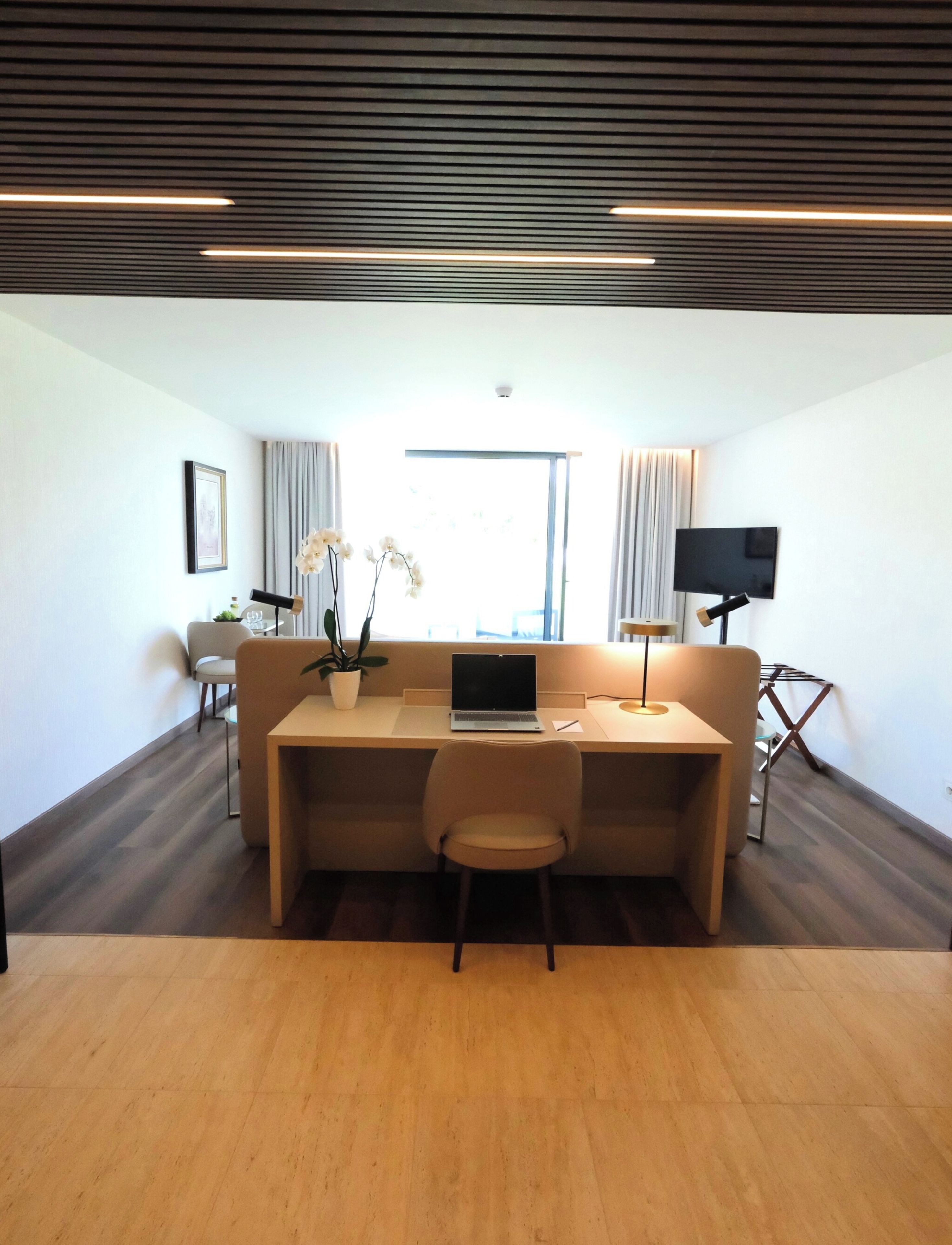 Una habitación moderna con piso de madera, un sofá, un escritorio con una computadora portátil, un televisor y una ventana con cortinas.