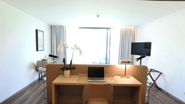 A modern room with a wooden floor, a sofa, a desk with a laptop, a TV, and a window with curtains. - Quinta Da Maquia Hotel (Sintra)