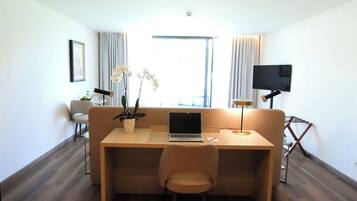 Una habitación moderna con piso de madera, un sofá, un escritorio con una computadora portátil, un televisor y una ventana con cortinas.