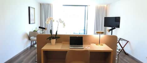 Una habitación moderna con piso de madera, un sofá, un escritorio con una computadora portátil, un televisor y una ventana con cortinas.