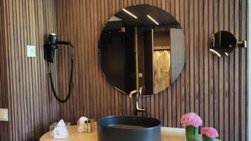 A modern bathroom with a wooden panel wall, a round mirror, a black sink, and a towel rack.