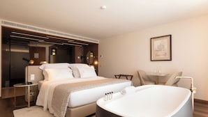 A modern hotel room with a large bed, a bathtub, a small table, and a chair. - Quinta Da Maquia Hotel (Sintra)