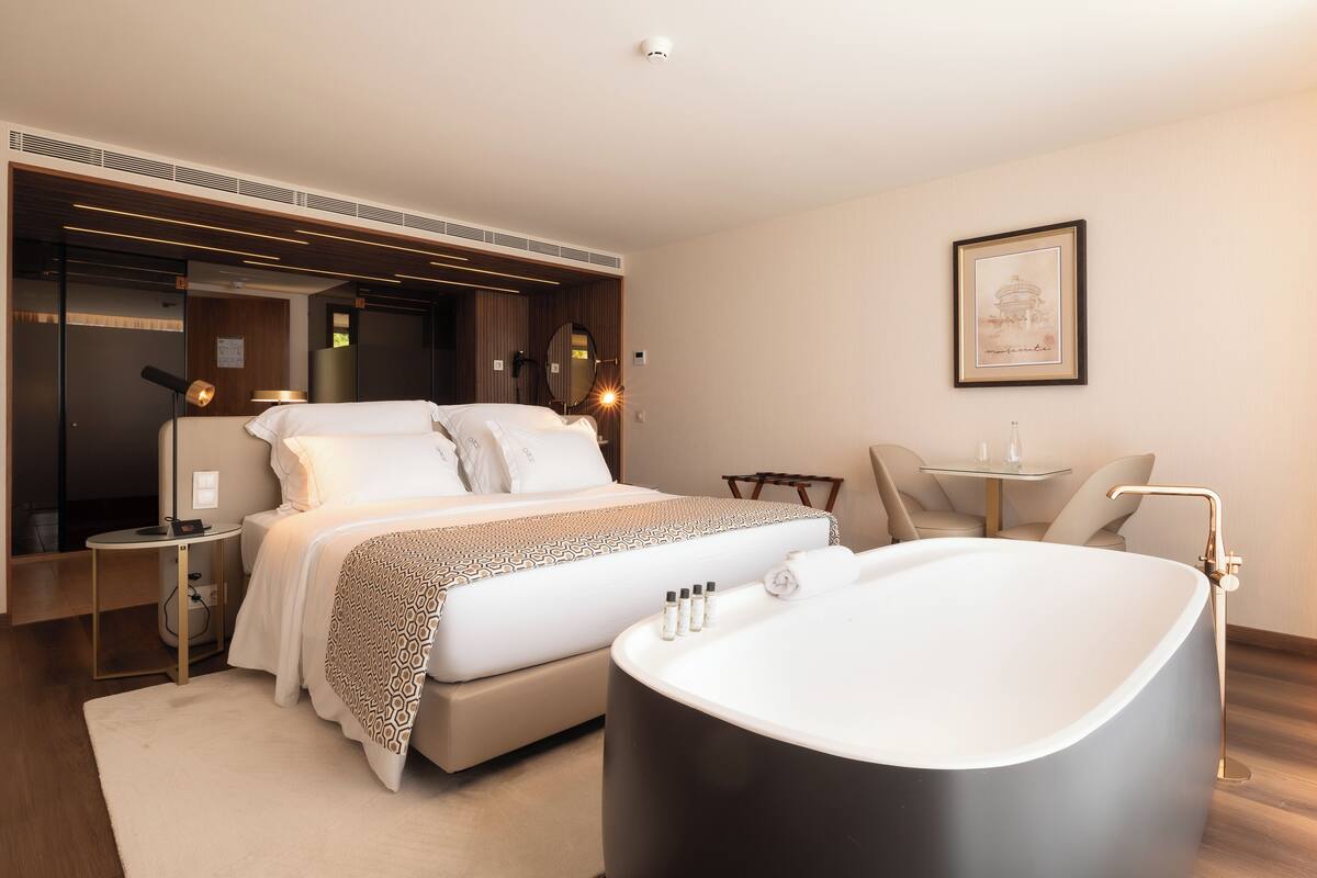 Ein modernes Hotelzimmer mit einem großen Bett, einer Badewanne, einem kleinen Tisch und einem Sessel.