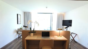 A modern room with a wooden floor, a sofa, a desk with a laptop, a TV, and a window with curtains. - Quinta Da Maquia Hotel (Sintra)