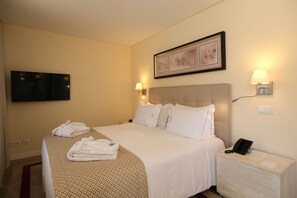 A hotel room with a bed, a bedside table with a phone, a wall-mounted TV, and two wall sconces. - Quinta Da Maquia Hotel (Sintra)