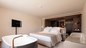 A modern hotel room with a large bathtub, a bed with a patterned bedspread, a glass coffee table, and a flat-screen TV mounted on the wall. - Quinta Da Maquia Hotel (Sintra)