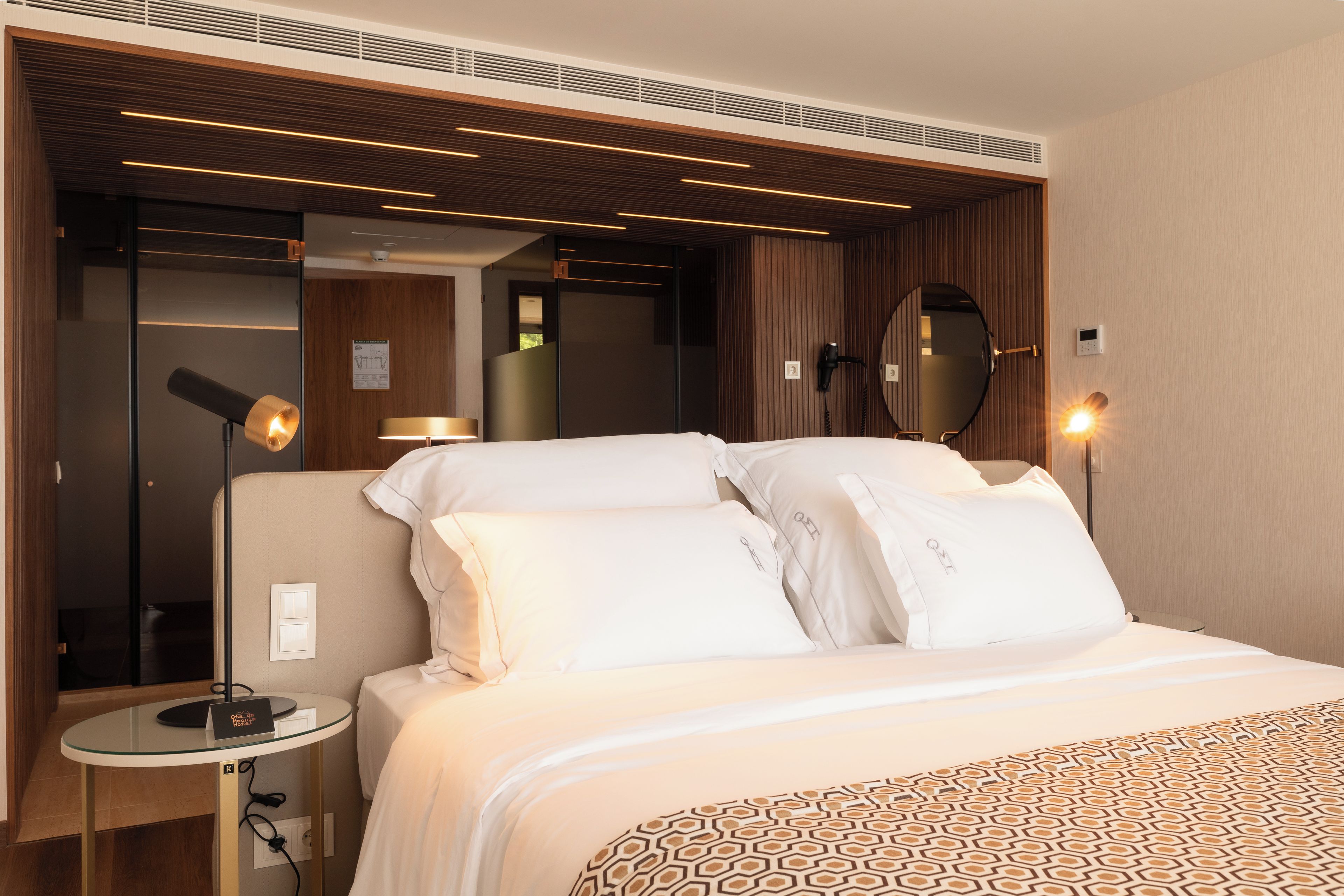 Una habitación de hotel moderna con una cama bien hecha, un espejo redondo y dos lámparas de noche.