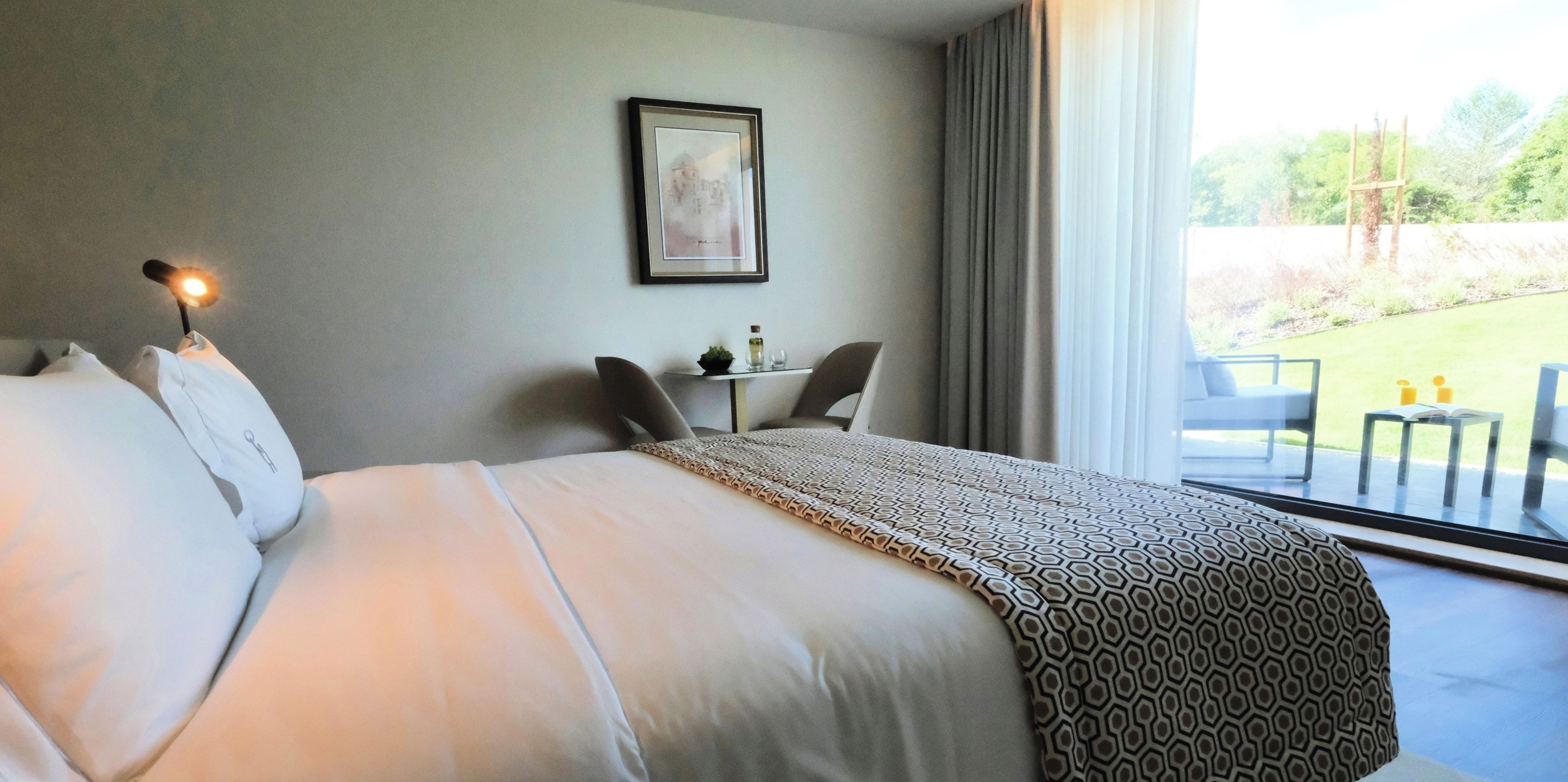 Ett hotellrum med en stor säng, ett skrivbord med en stol, en inramad tavla på väggen och utsikt över omgivningarna.