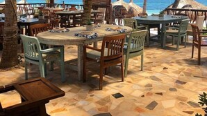 Un área de comedor al aire libre con mesas y sillas, palmeras y vistas al océano.