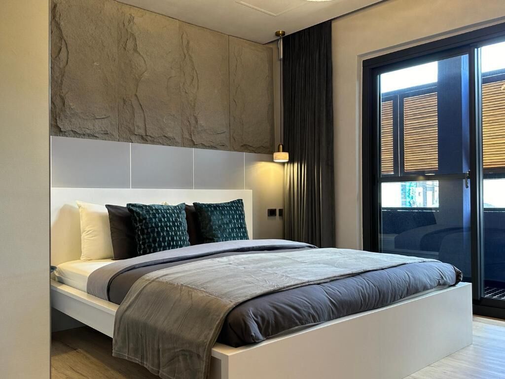 Un dormitorio moderno con una cama grande, una pared de acento de piedra y vistas a través de un ventanal.