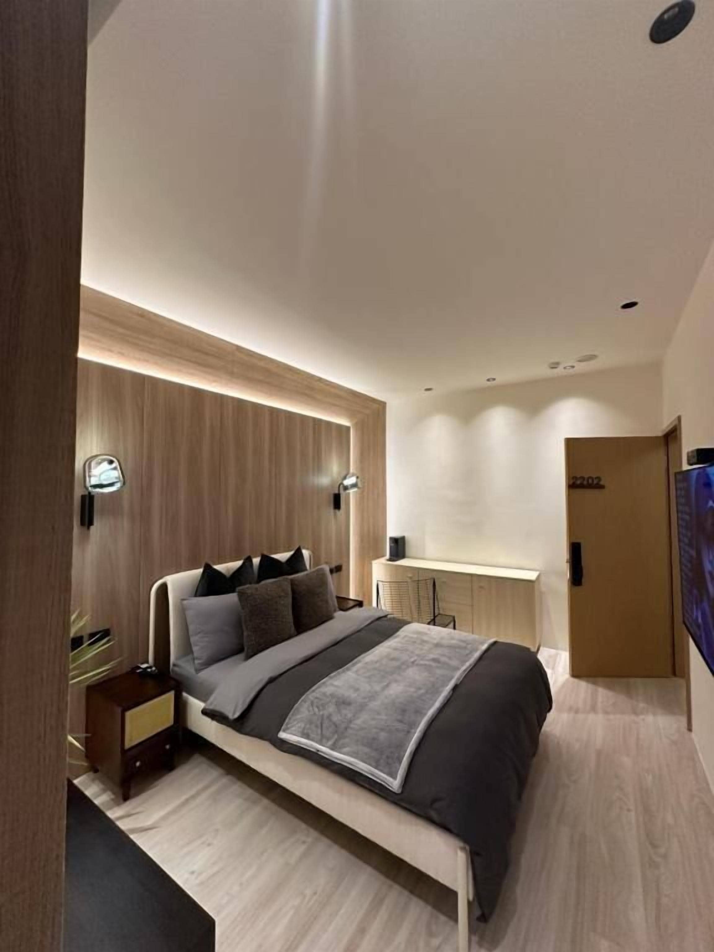 A modern bedroom with a bed, bedside tables, a desk, and a TV.