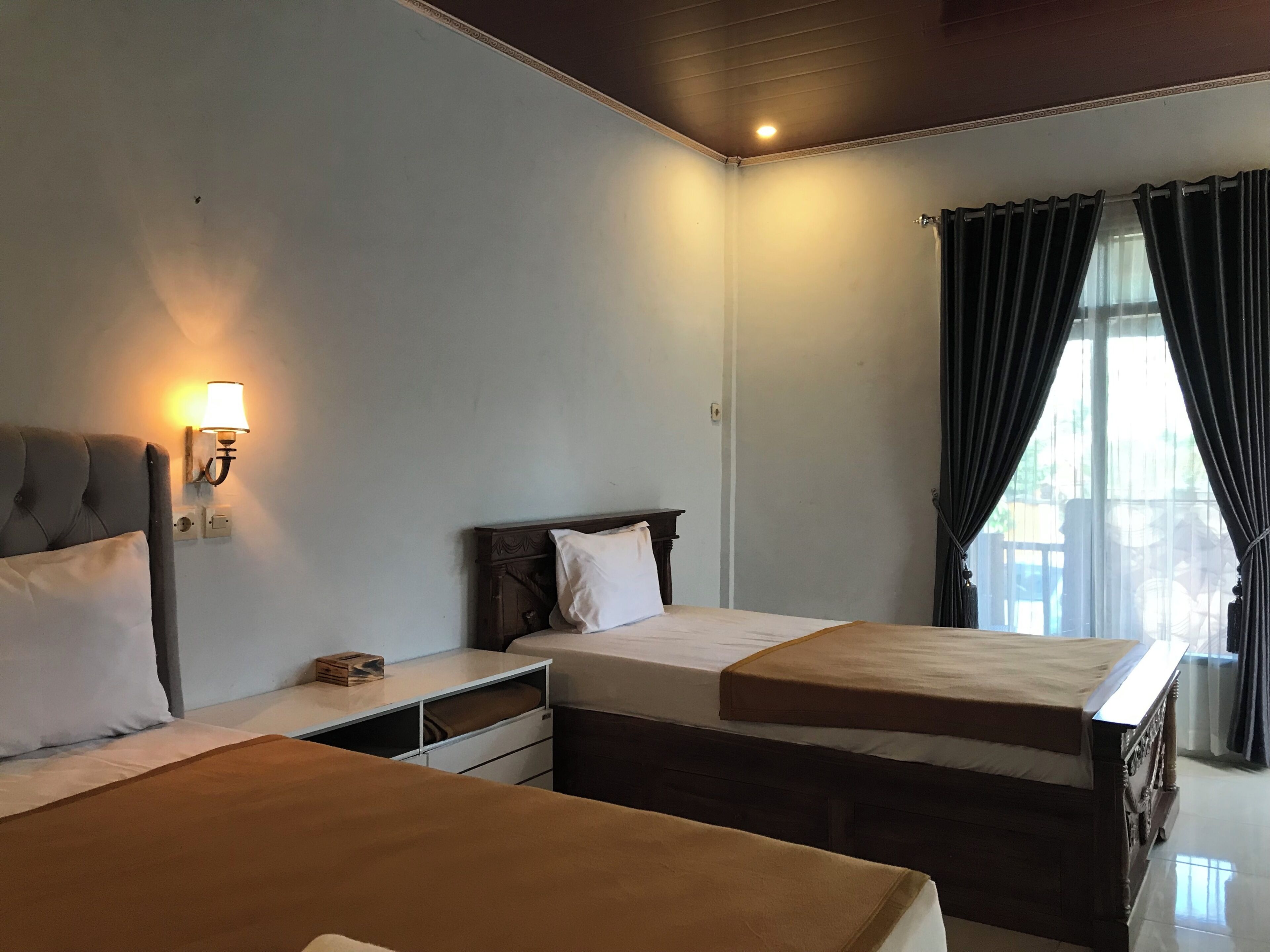 Une chambre d’hôtel avec deux lits, une table de chevet, une lampe et une fenêtre avec des rideaux.