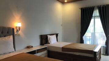 Une chambre d’hôtel avec deux lits, une table de chevet, une lampe et une fenêtre avec des rideaux.