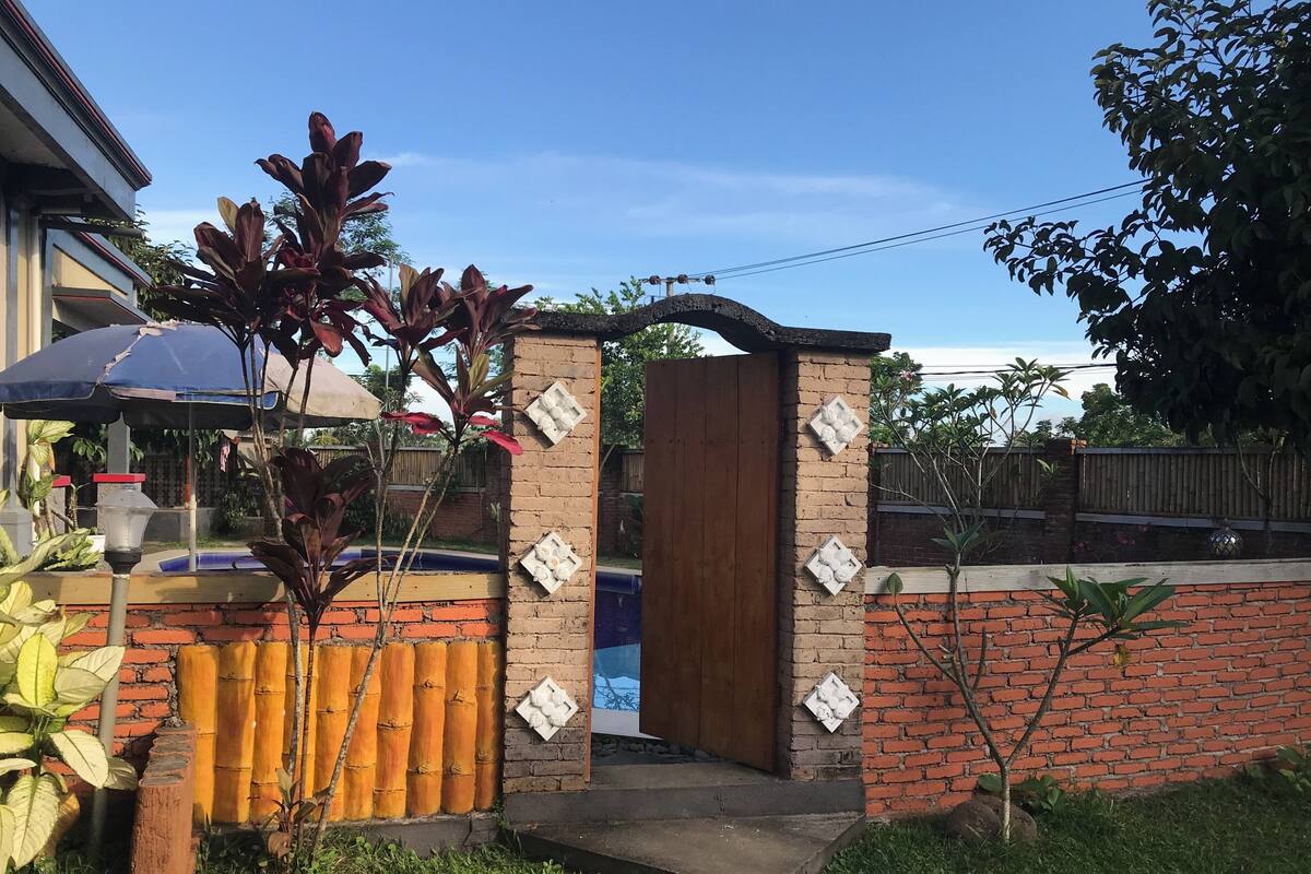 Tiiliseinä, jossa on puuovi, bambuaita ja pieni puutarha-alue, jossa on kasveja.