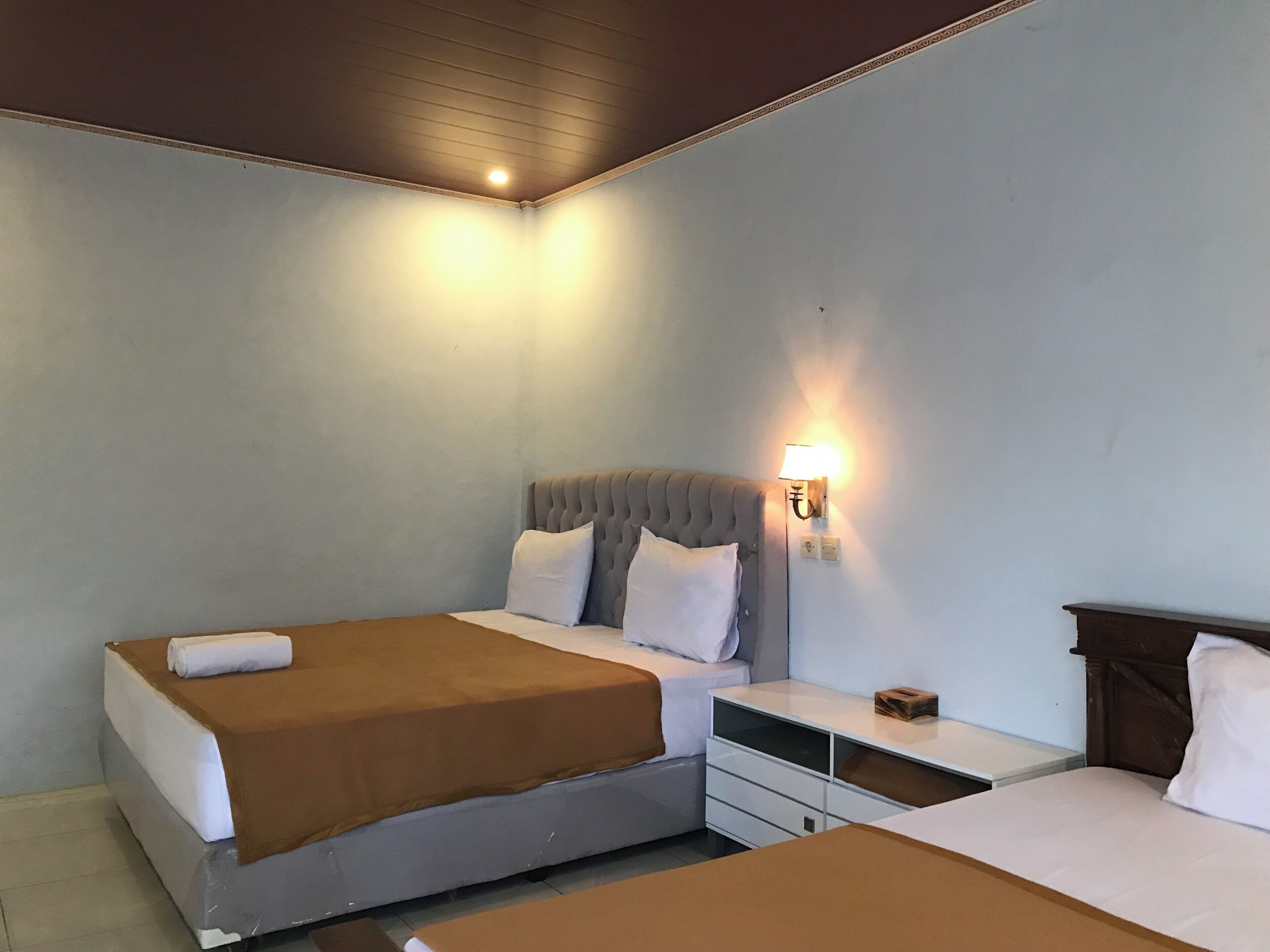 A hotel room with two beds, a bedside table, a lamp, and a ceiling light.