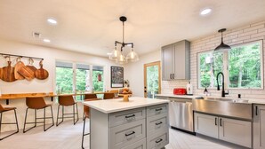 A modern kitchen with a central island, bar stools, and a view of greenery outside. - Biltmore Forest Retreat! Sauna Hot tub Game Rm (Asheville)