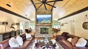 A spacious living room with leather sofas, a stone fireplace, and a large TV screen. - Biltmore Forest Retreat! Sauna Hot tub Game Rm (Asheville)