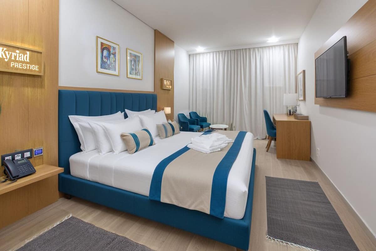 Ein Hotelzimmer mit einem großen Bett, einem Schreibtisch, einem Stuhl, einem Fernseher und Kunstwerken an den Wänden.