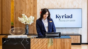 Een receptiebalie met een naambordje, een vaas met witte bloemen, en een bordje met de tekst 'Kyriad Prestige City Center'.