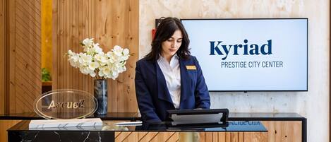 A reception desk with a nameplate, a vase with white flowers, and a sign reading "Kyriad Prestige City Center".