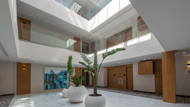 Een moderne hotellobby met een hoge plafond, glazen balustrades en grote potplanten.