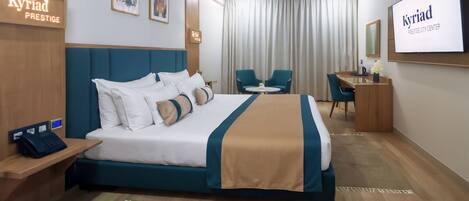 A hotel room with a large bed, a desk, two chairs, a TV, and artwork on the walls.