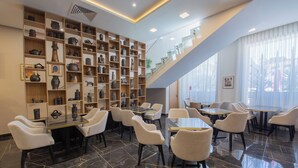 Een moderne hotel lobby met een glazen trap, diverse decoratieve items op planken, en een zithoek met tafels en stoelen.