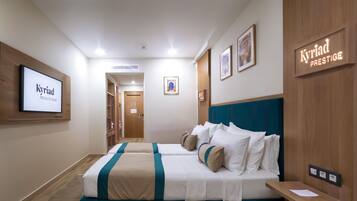 Habitación de hotel con una cama grande, un escritorio y un armario. Hay cuadros en las paredes y un letrero que dice "Kyriad Prestige".